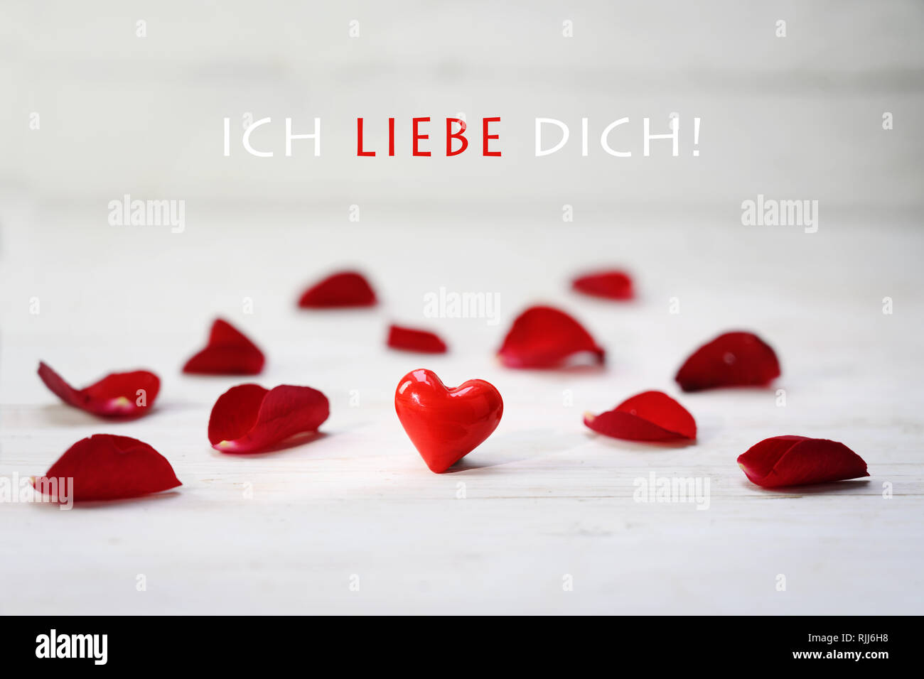 Coeur en verre rouge entre des pétales de rose sur un fond de bois gris clair, texte allemand ich liebe dich, qui signifie "je t'aime, de mise au point sélectionnée, la profondeur de l'étroit Banque D'Images