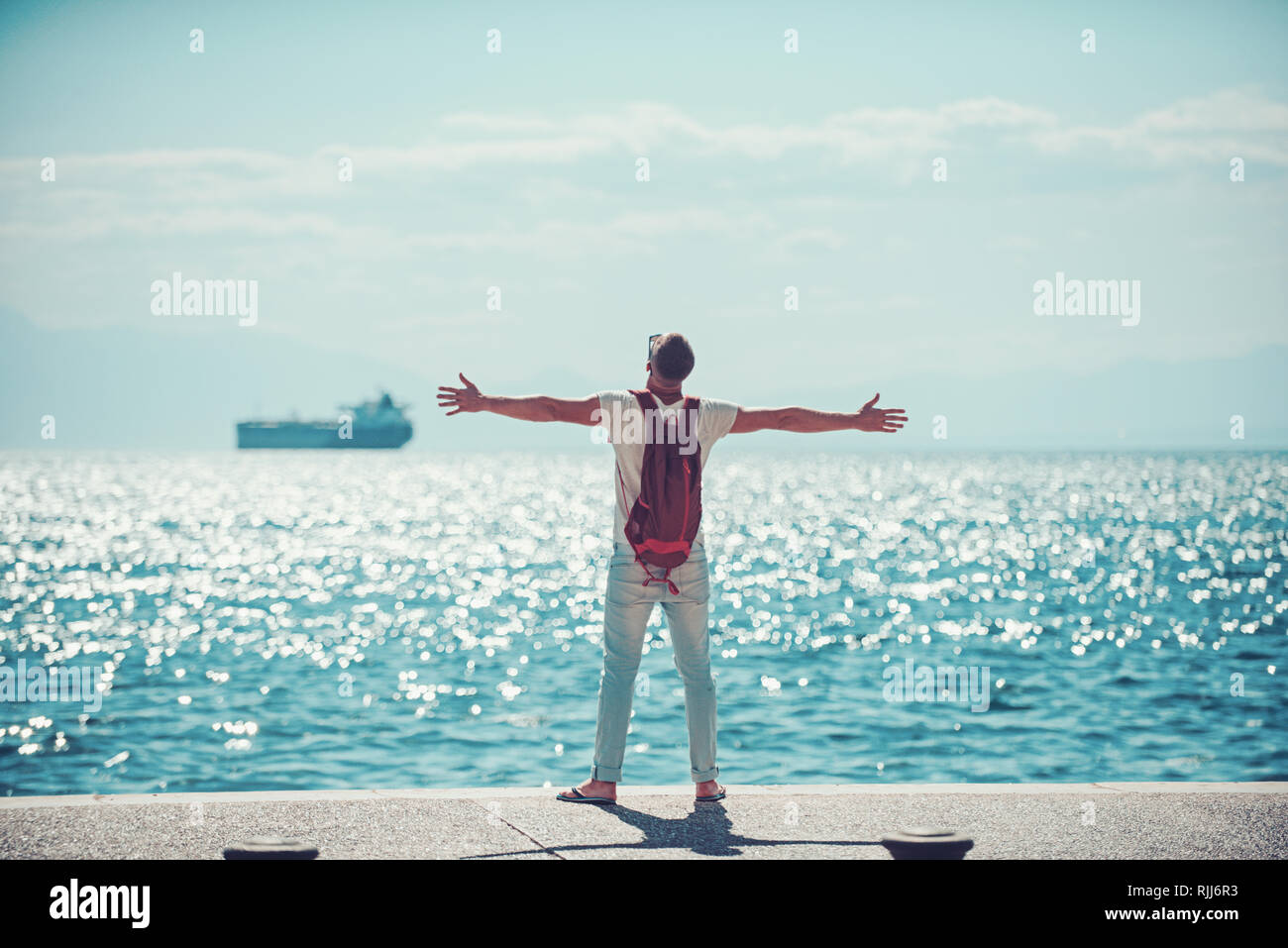 Voyageur avec sac à dos homme tenir levé les mains à l'eau de mer. Voyages et vacances d'été. concept wanderlust et aventures. Jeune homme va à marine Banque D'Images