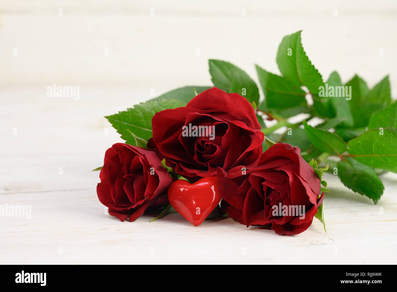 Trois roses rouges et un cœur de verre sur un fond de bois blanc, l'amour concept avec copie espace étroit, de mise au point sélectionnée, la profondeur de champ Banque D'Images