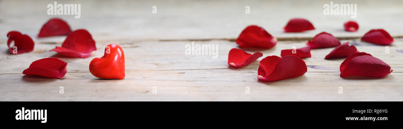 Coeur rouge en verre et des pétales de rose sur une planche en bois rustique, de l'amour concept avec copie espace, en format panoramique, bannière mise au point sélectionné, étroite d Banque D'Images