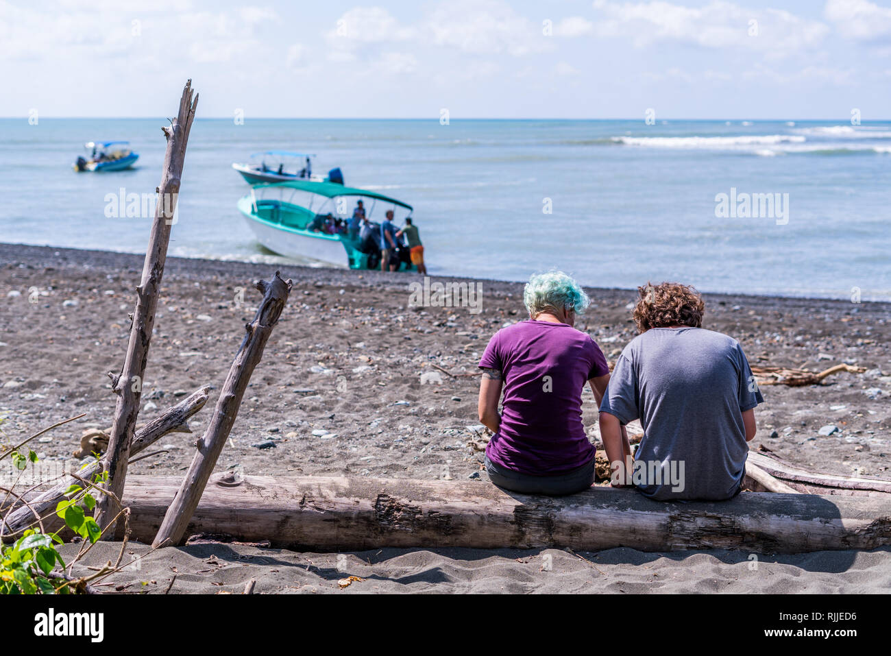 Deux touristes se détendre sur une grosse dérive du journal à terre sur la magnifique plage de parc national Corcovado, Costa Rica. Bateau sur l'arrière-plan. Banque D'Images