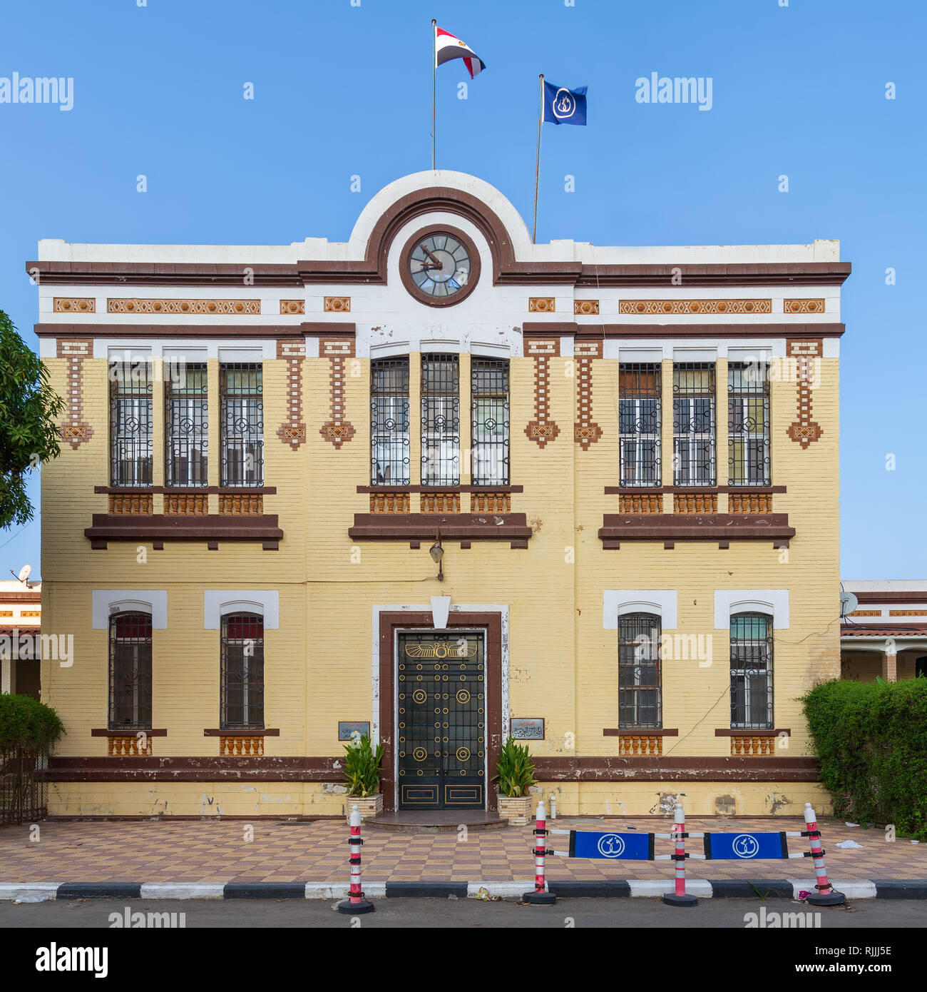 Façade d'affaires financières de l'Autorité du Canal de Suez avec briques jaunes, porte simple, windows couverts avec des barres de fer, et de l'horloge Banque D'Images