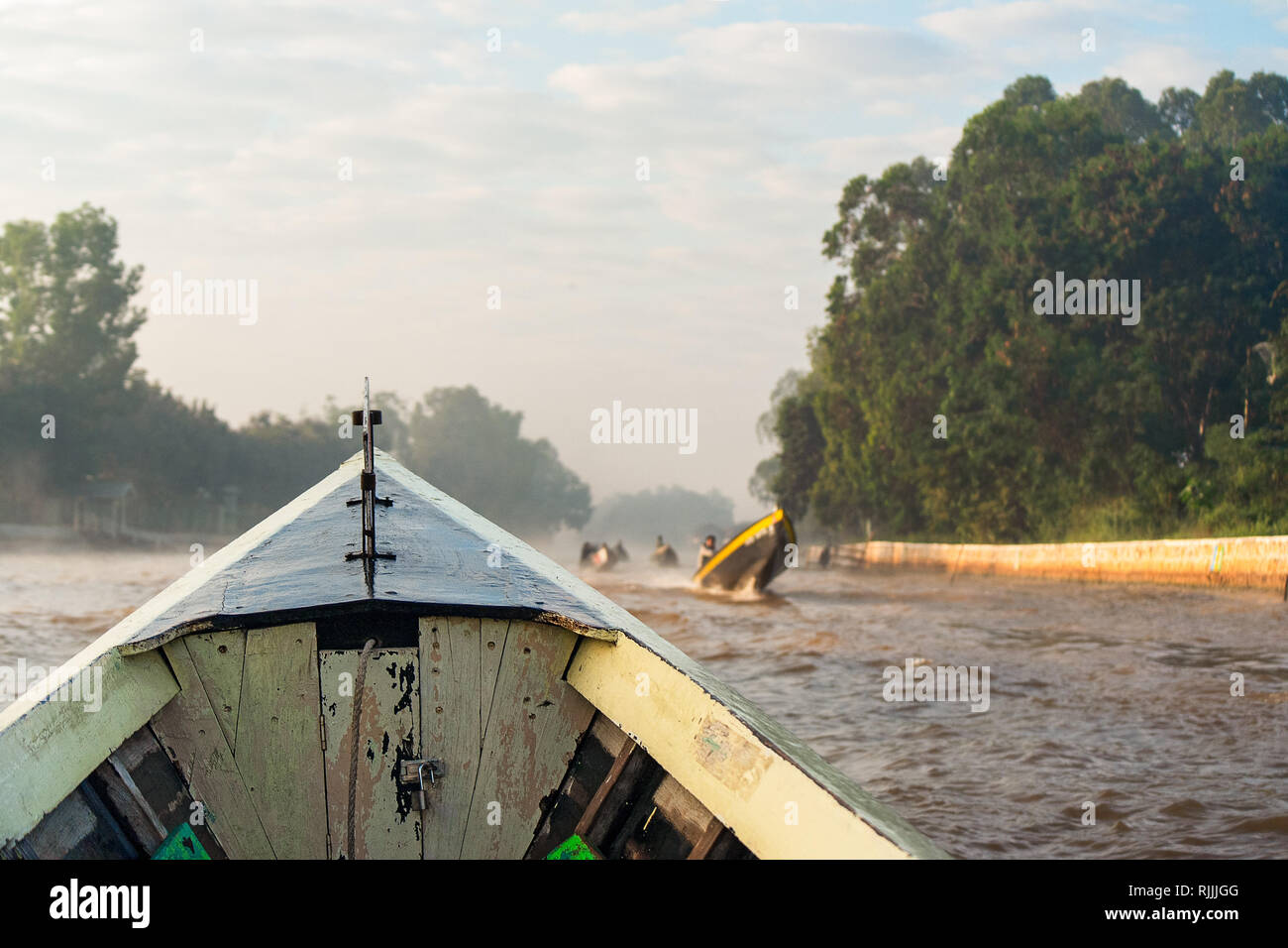 Proue d'un bateau en bois mène une longue une rivière agitée de paroisses au Lac Inle, Myanmar. Banque D'Images