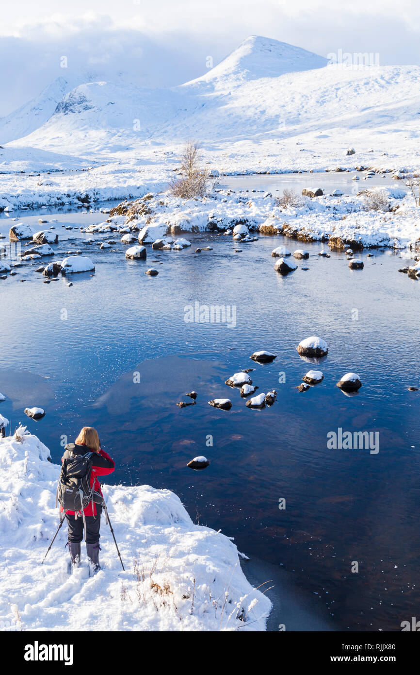Femme de prendre des photos lors d'une froide après-midi d'hiver avec la neige et le loch partiellement gelé dans le Loch Rannoch Moor, Ba, l'Argyll and Bute en Janvier Banque D'Images