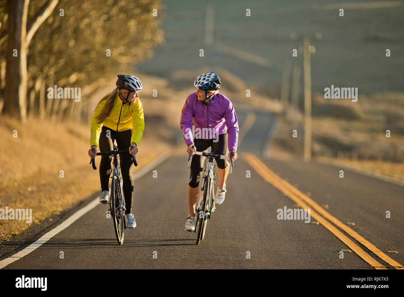 Deux jeunes femmes sourire ensemble à vélo vers le bas une route de campagne. Banque D'Images
