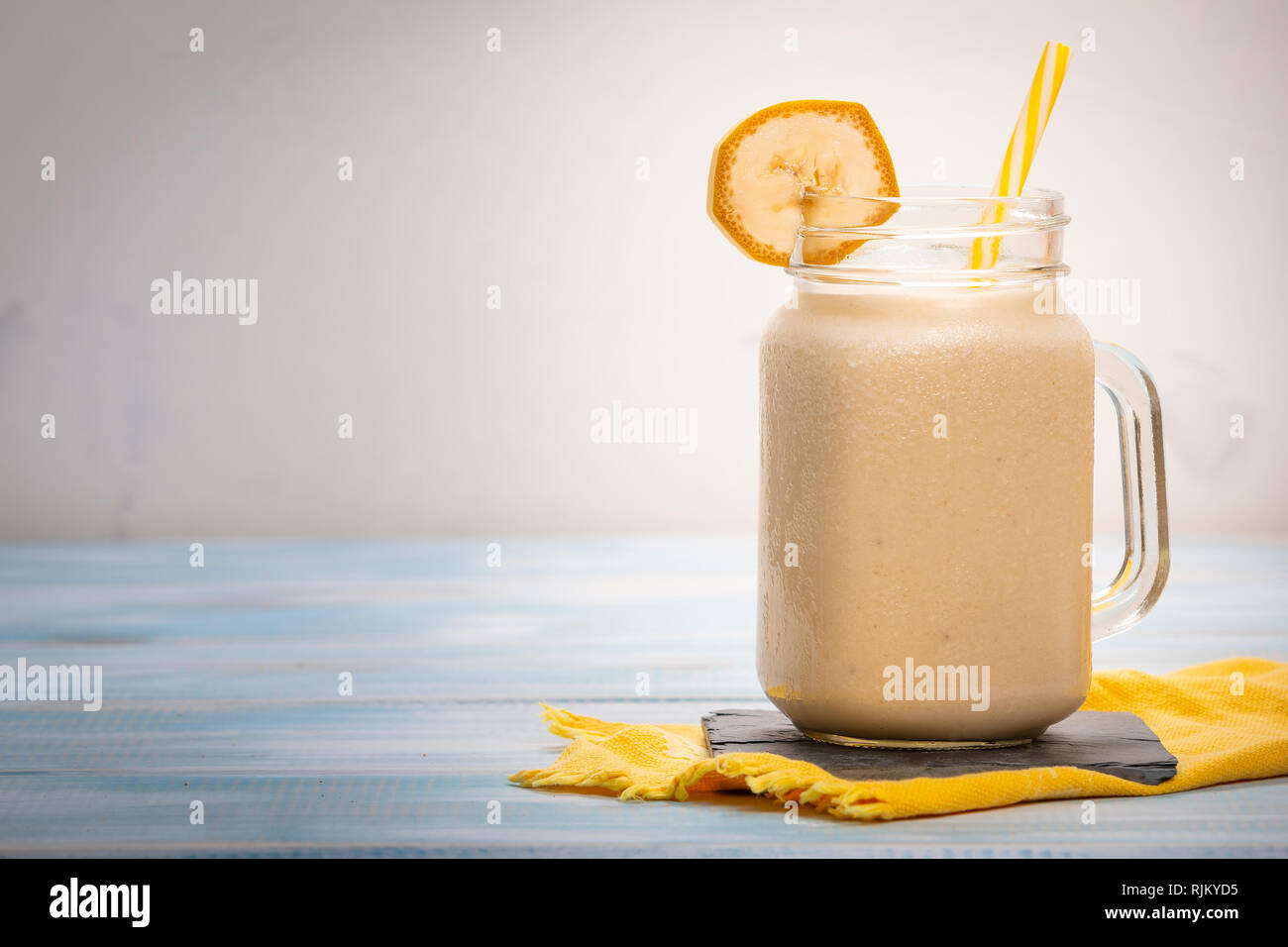 Délicieux boisson fraîche dans le verre mug sur le tube en plastique et des tranches de banane sur serviette sur table en bois Banque D'Images