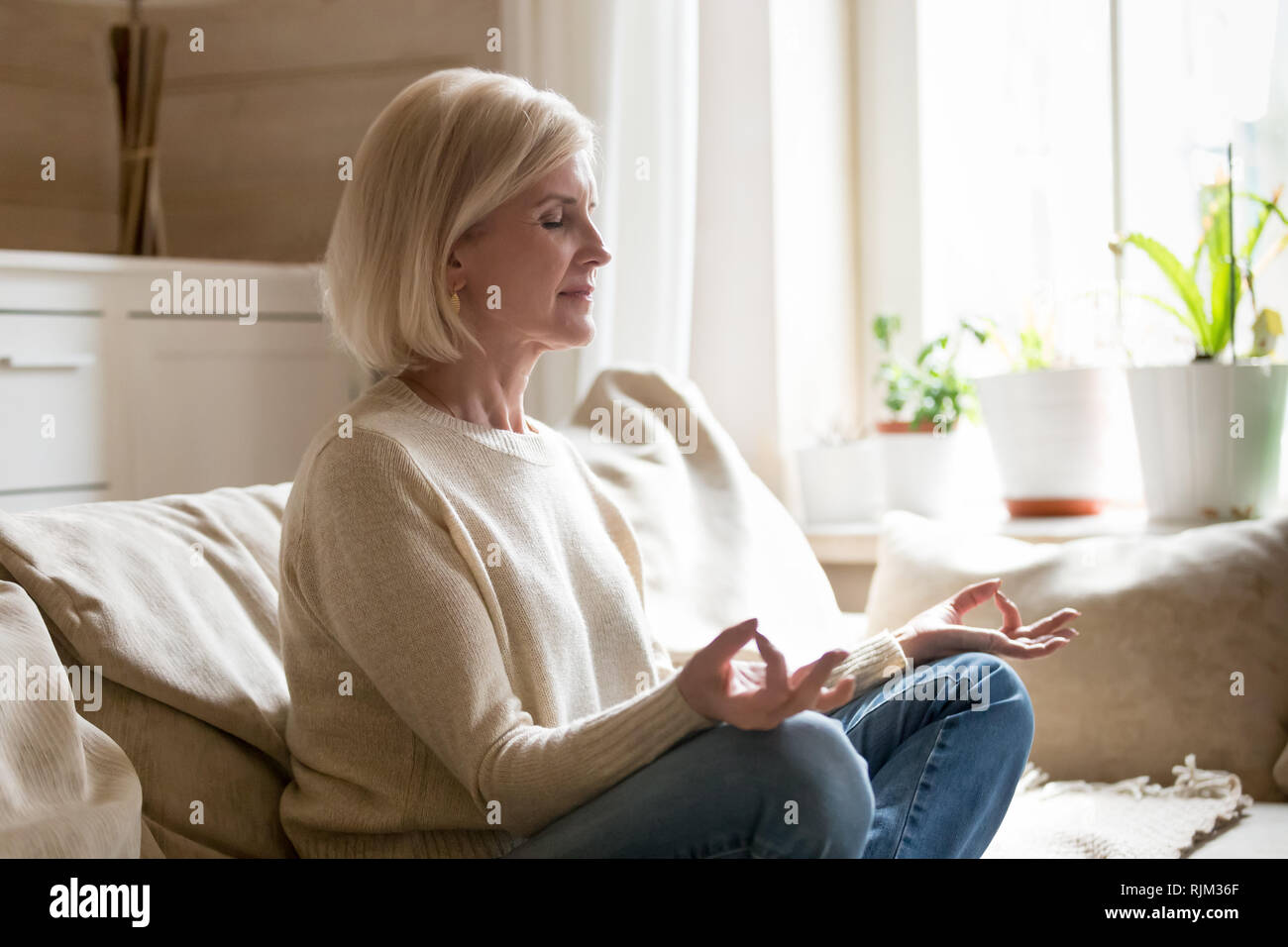 Femelle adulte assis en position du lotus faisant du yoga à la maison Banque D'Images