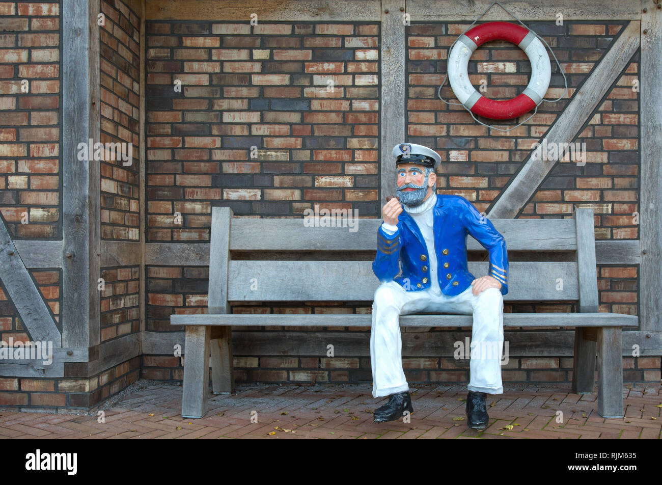 Un marin avec tuyau et est assis sur un banc en face d'un mur de pierre Banque D'Images