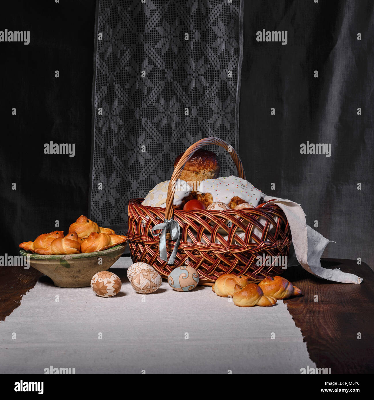 Panier de pâques avec de la nourriture et un bol avec des brioches, des oiseaux et des œufs sont sur la table par l'éclairage discret contre le rituel de l'Ukraine. Banque D'Images