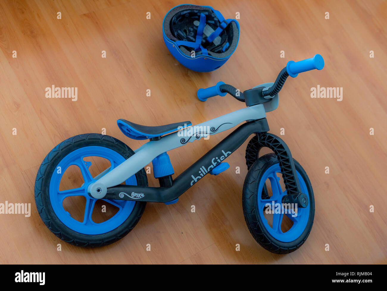 Une belle photo d'un BMXie Chillafish balance bike par avec un beau casque bleu couché sur un plancher en bois. Banque D'Images