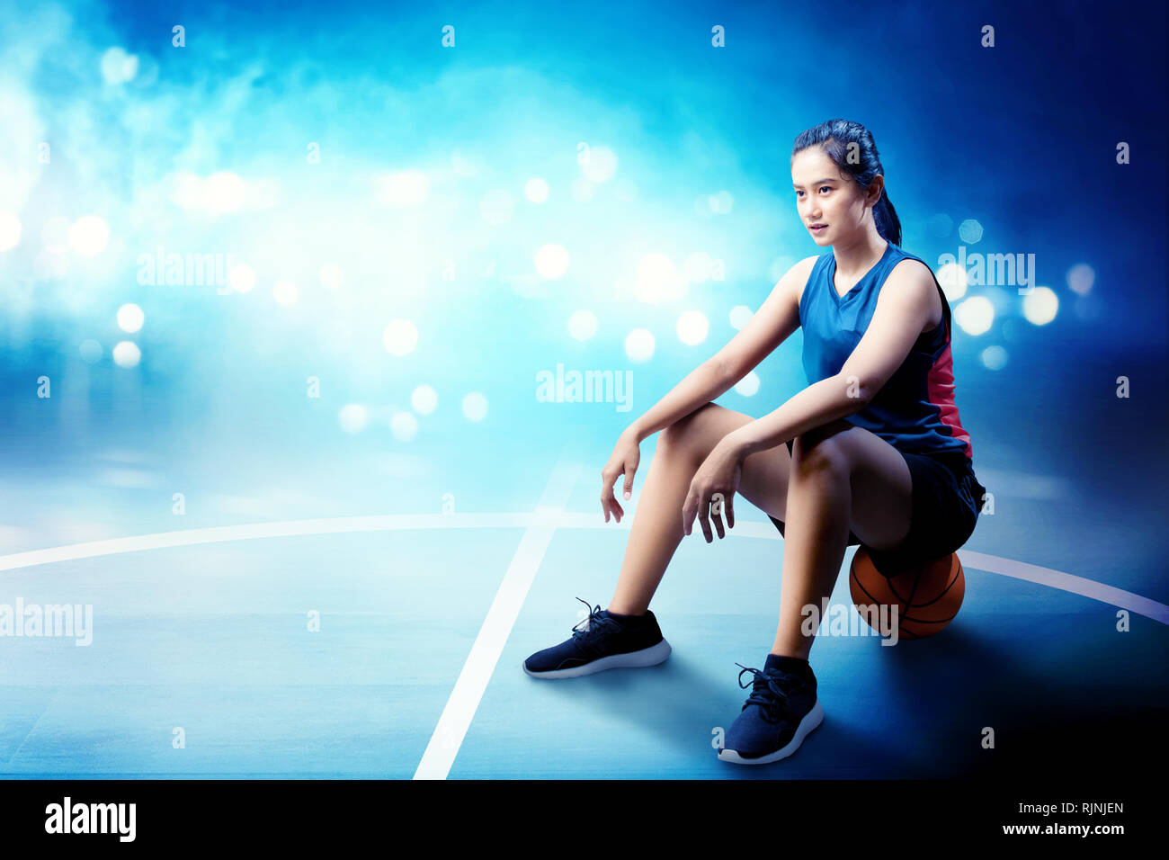Joueur de basket-ball Smiling asian woman sitting on the ball en basket-ball Banque D'Images