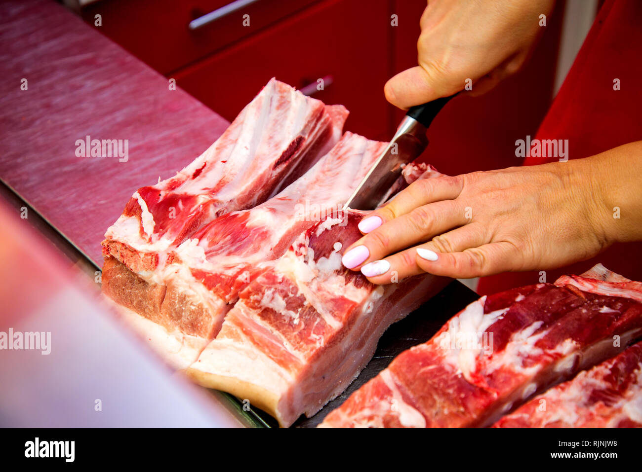 Coupe femme boucher morceau de viande de côtes dans sa boutique avec un couteau. Banque D'Images