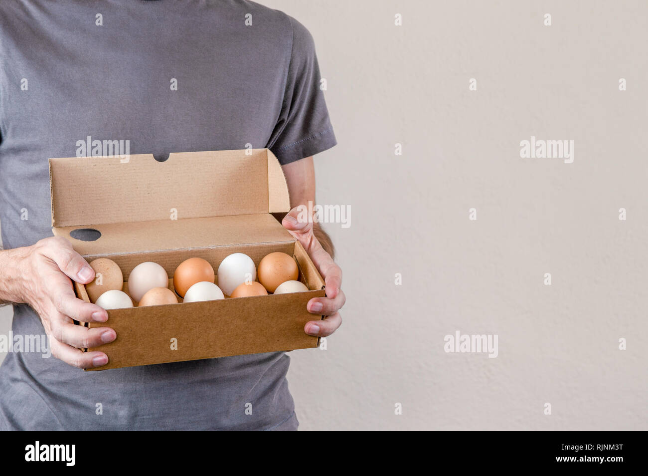 Caucasian man with Grey T-shirt tenant un oeuf en carton boîte pleine d'oeufs de poule sur un fond blanc. Banque D'Images