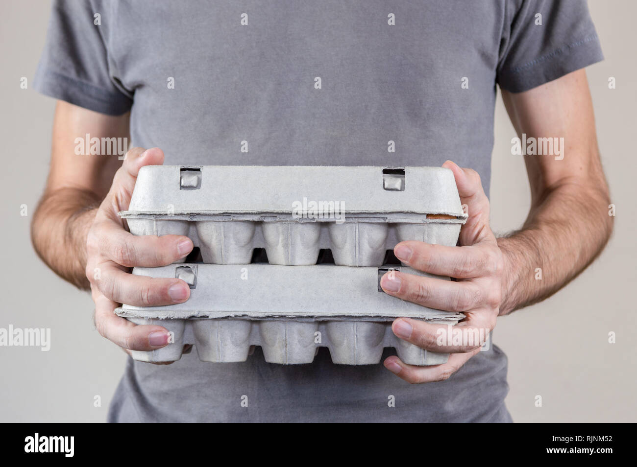 Caucasian man with Grey T-shirt tenant deux boîtes d'oeufs en carton plein d'œufs de poule sur un fond blanc. Banque D'Images