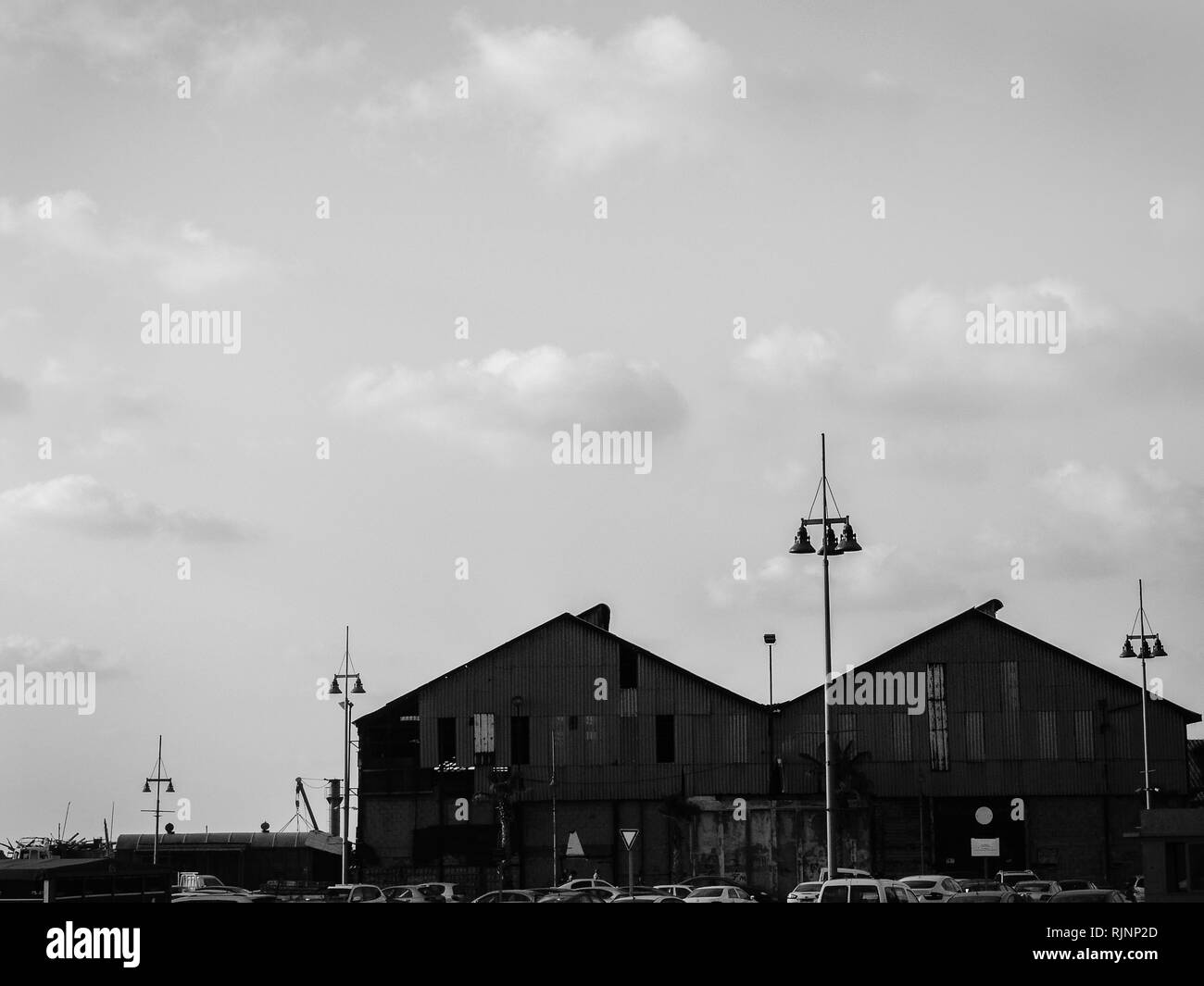 Vue urbaine en noir et blanc de deux toits de grands bâtiments par le port de mer, bateaux avec de grandes lampes de la ville à l'avant, sous ciel nuageux. Banque D'Images