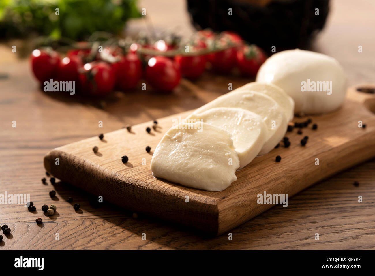 Le mozzarella sur planche en bois. Tomates cerises en arrière-plan. Table en bois avec la composition des aliments italiens Banque D'Images