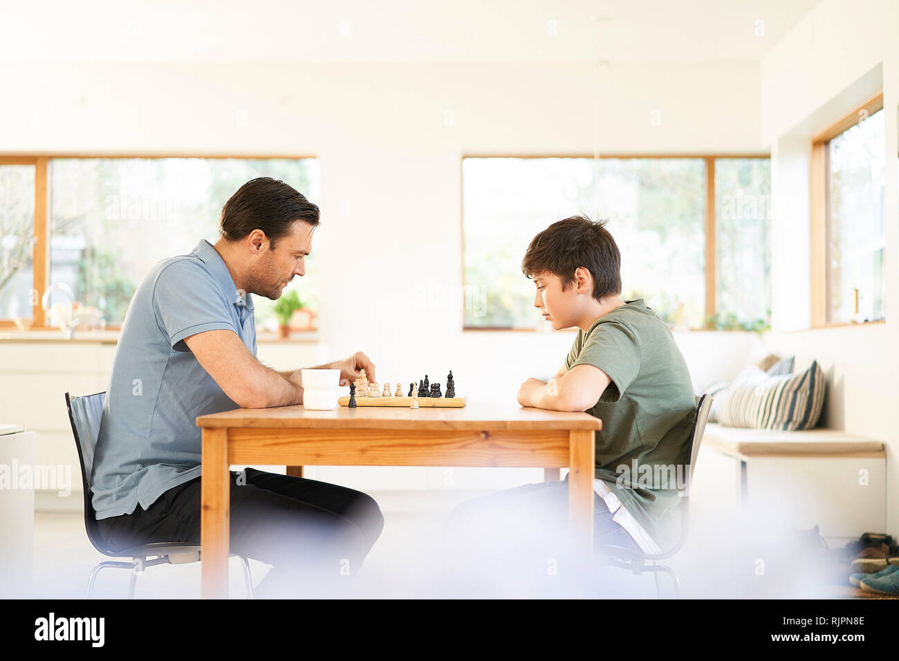 Garçon et père jouer aux échecs à table de salon Banque D'Images