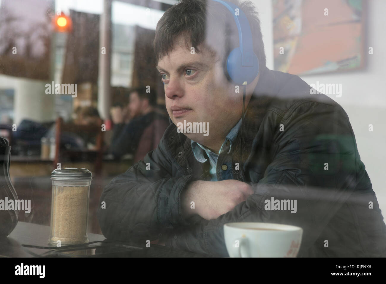 L'homme avec le syndrome de l'aide d'écouteurs par fenêtre cafe Banque D'Images