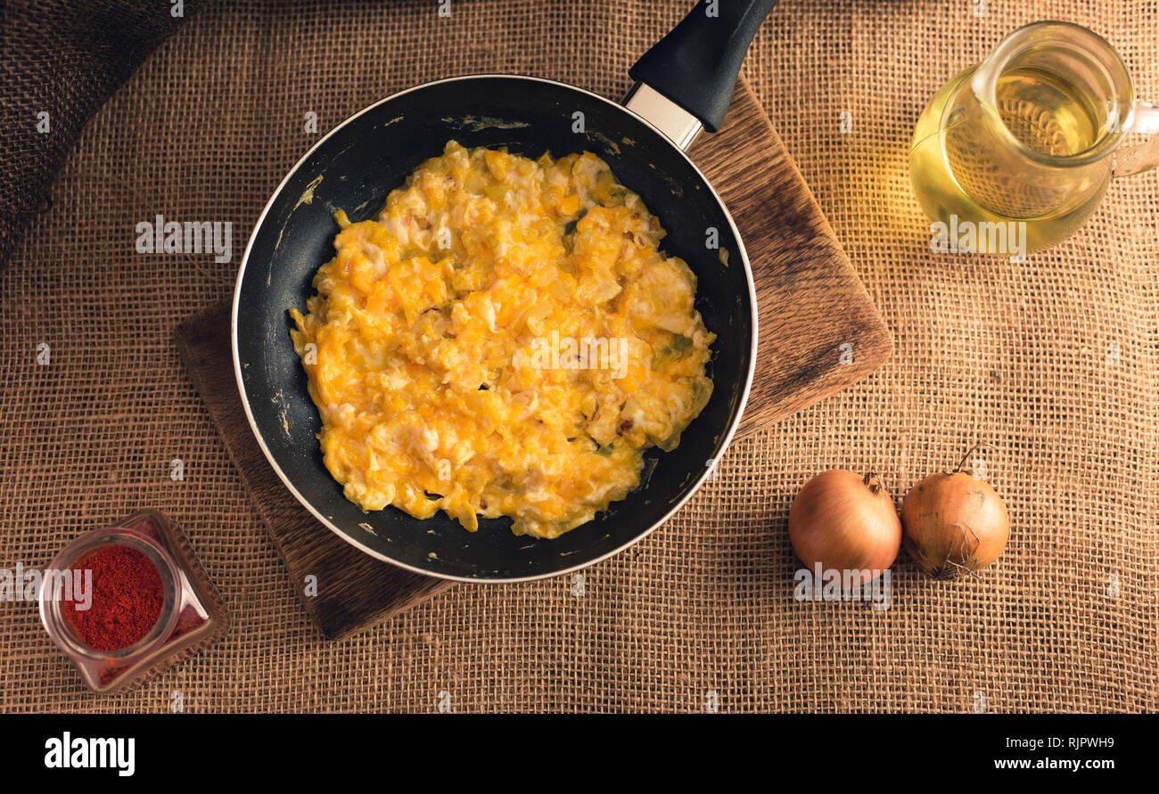 Photo des œufs brouillés avec du paprika, d'oignons et d'huile d'en haut - style rural. Le jaune des oeufs brouillés en noir sur fond de jute pan. Banque D'Images