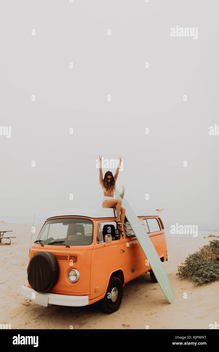 Les jeunes filles en bikini surfeur faisant signe de victoire de la partie supérieure du véhicule récréatif à Jalama, Beach, California, USA Banque D'Images