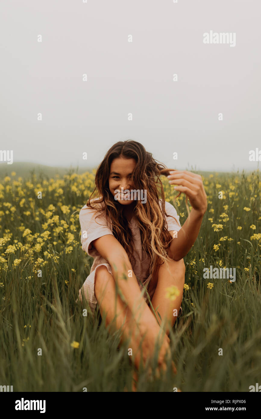 Jeune femme assise dans le champ de fleurs sauvages jaunes, portrait, Californie, Etats-Unis, Jalama Banque D'Images
