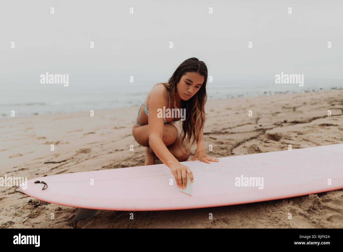Jeune femme surfer waxing with surfboard on beach, Ventura, Californie, USA Banque D'Images