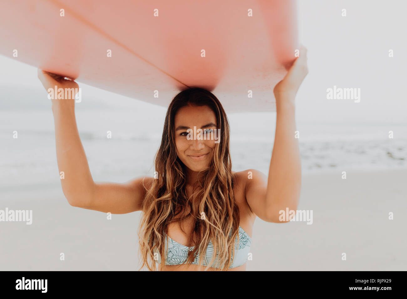 Jeune femme surfer carrying surfboard on beach à tête, portrait, Ventura, Californie, USA Banque D'Images