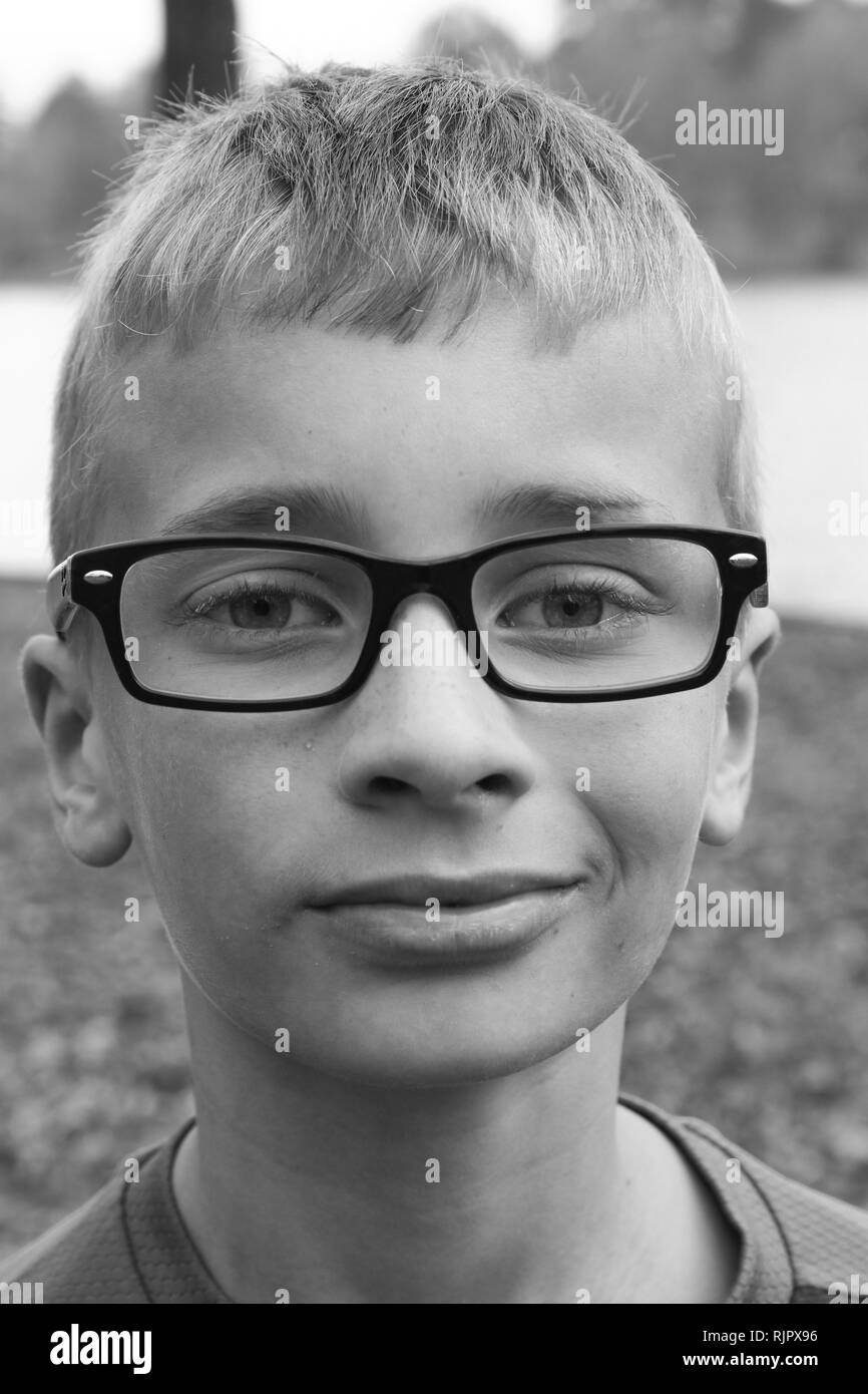 Portrait noir et blanc d'un garçon caucasien preteen avec des lunettes et un petit sourire narquois Banque D'Images