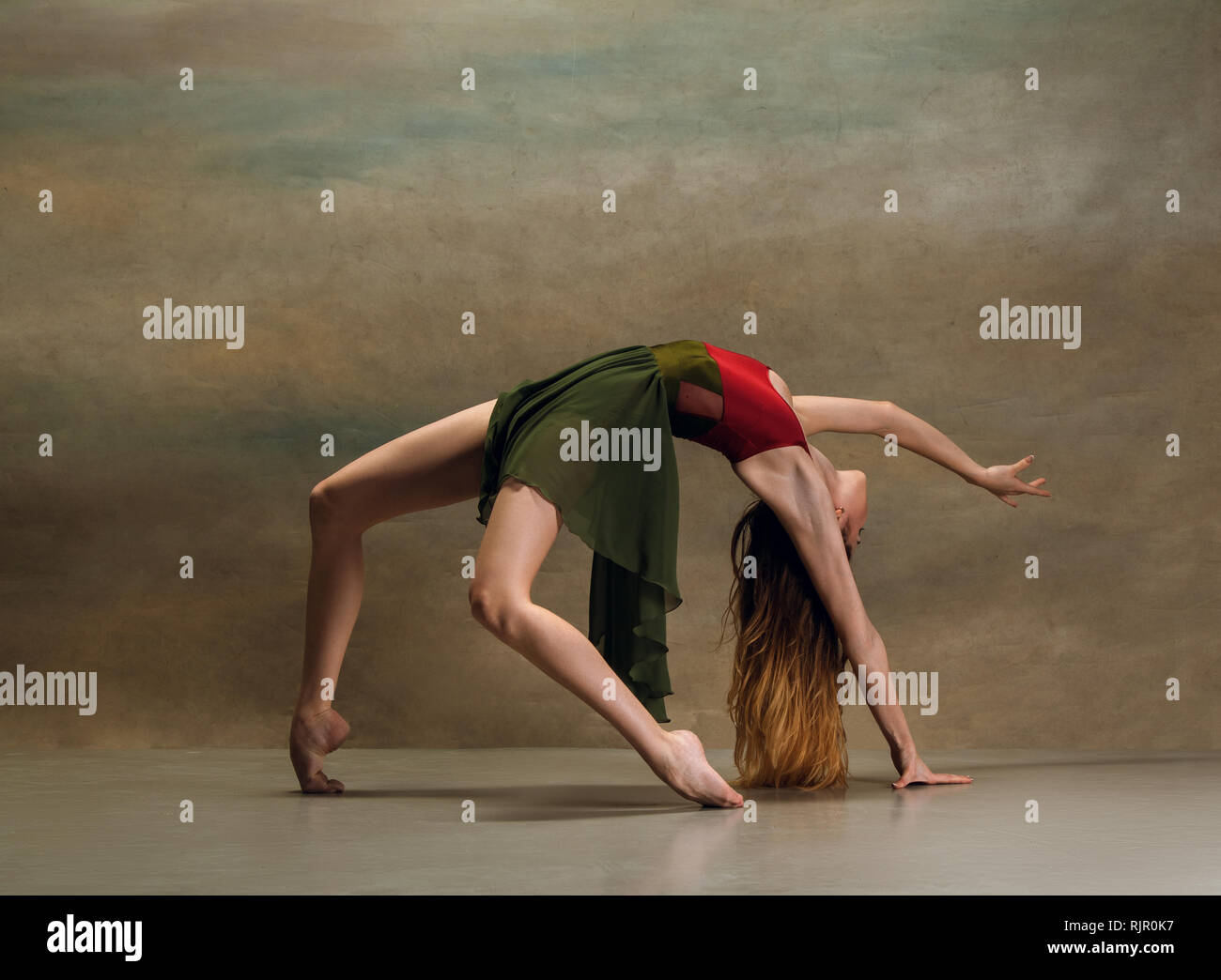 La jeune femme danse de style contemporain sur fond gris. Danseuse moderne au studio. L'élégance, la grâce et la performance concept Banque D'Images