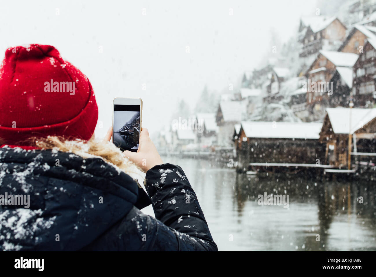 Woman in red hat prendre photo de lac de Hallstatt vieille ville pendant une tempête de neige, en Autriche. Banque D'Images