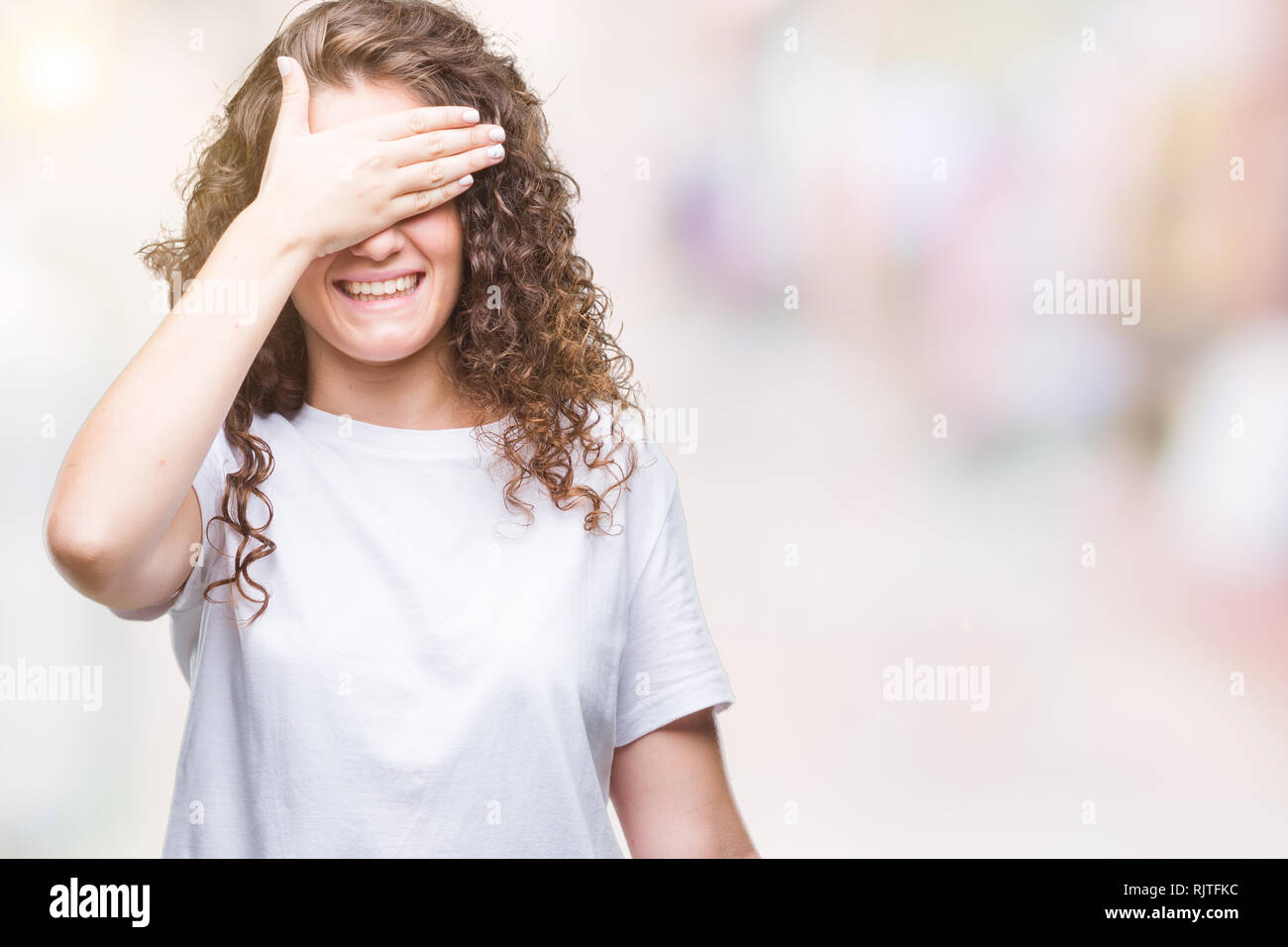 Belle brune cheveux bouclés jeune fille portant des T-shirt sur fond isolé sourire et rire avec la main sur le visage yeux couvrant pour surp Banque D'Images