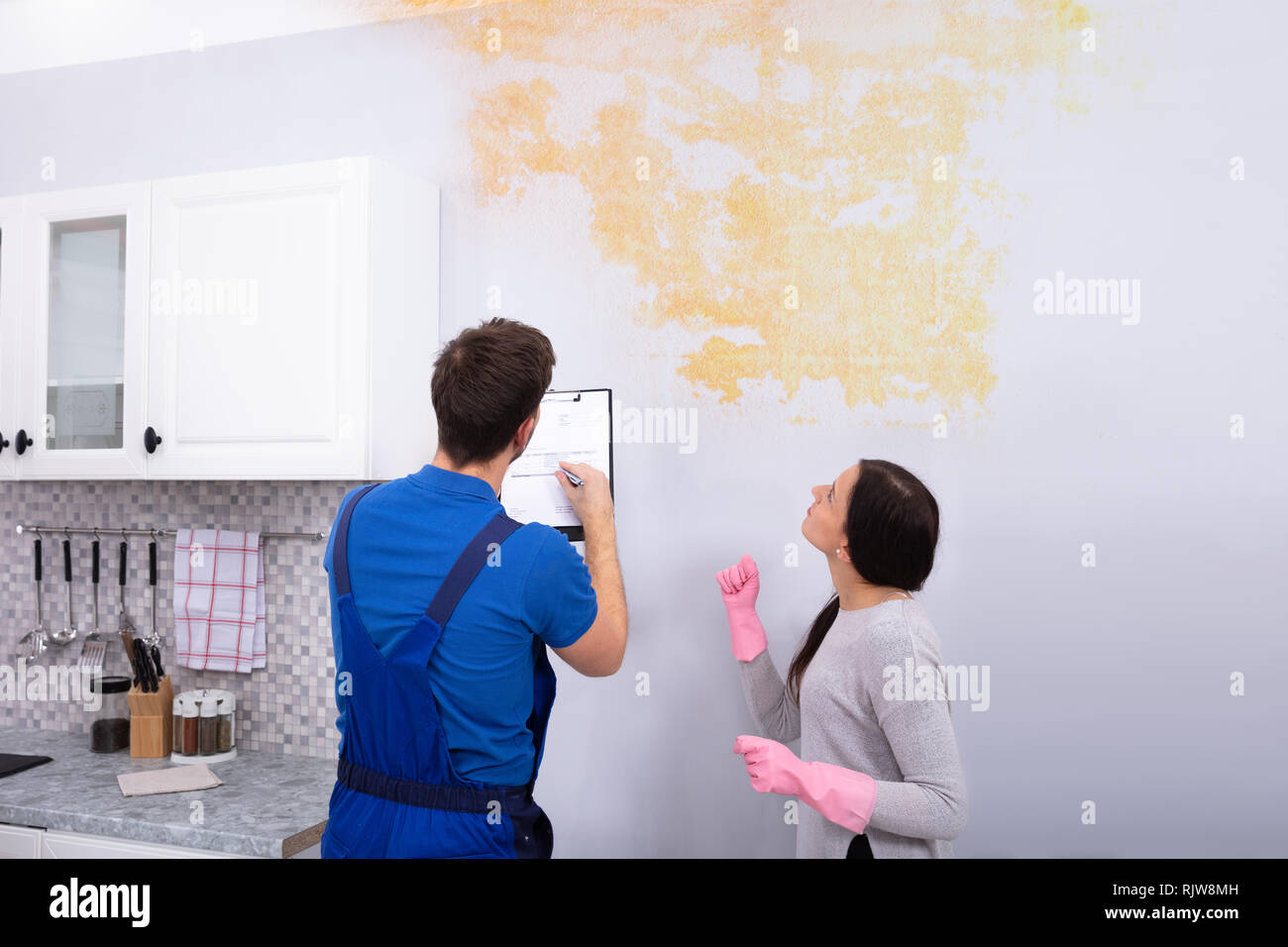 Young Worker Writing On Clipboard With Woman Standing In Kitchen Banque D'Images