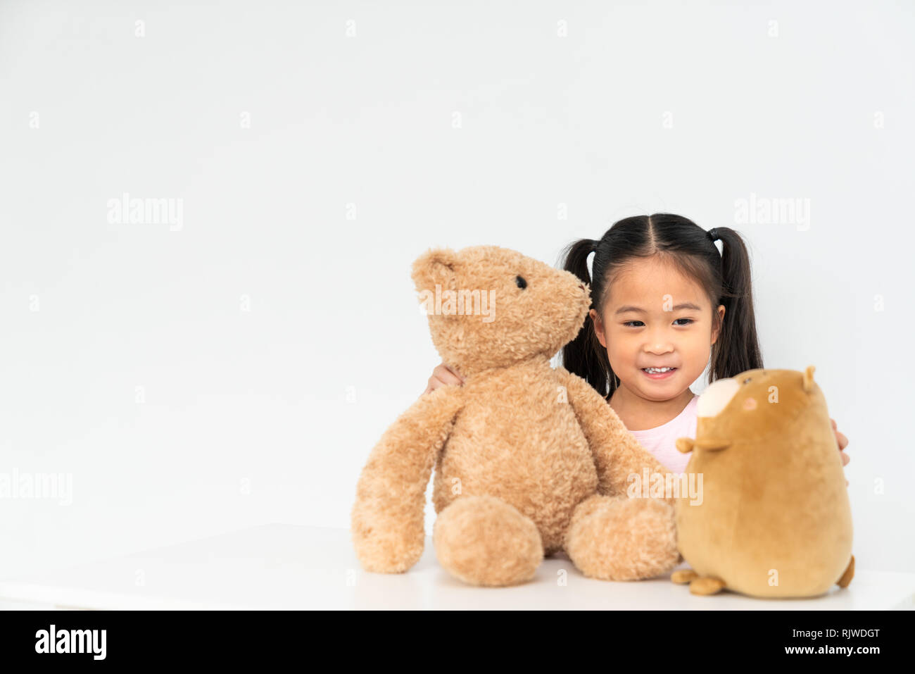 Belle jeune fille asiatique jouant avec 2 poupées en peluche mignon à la maison, l'espace de copie sur mur blanc arrière-plan. Un jeu d'enfant, de la petite enfance jeunesse activité Banque D'Images