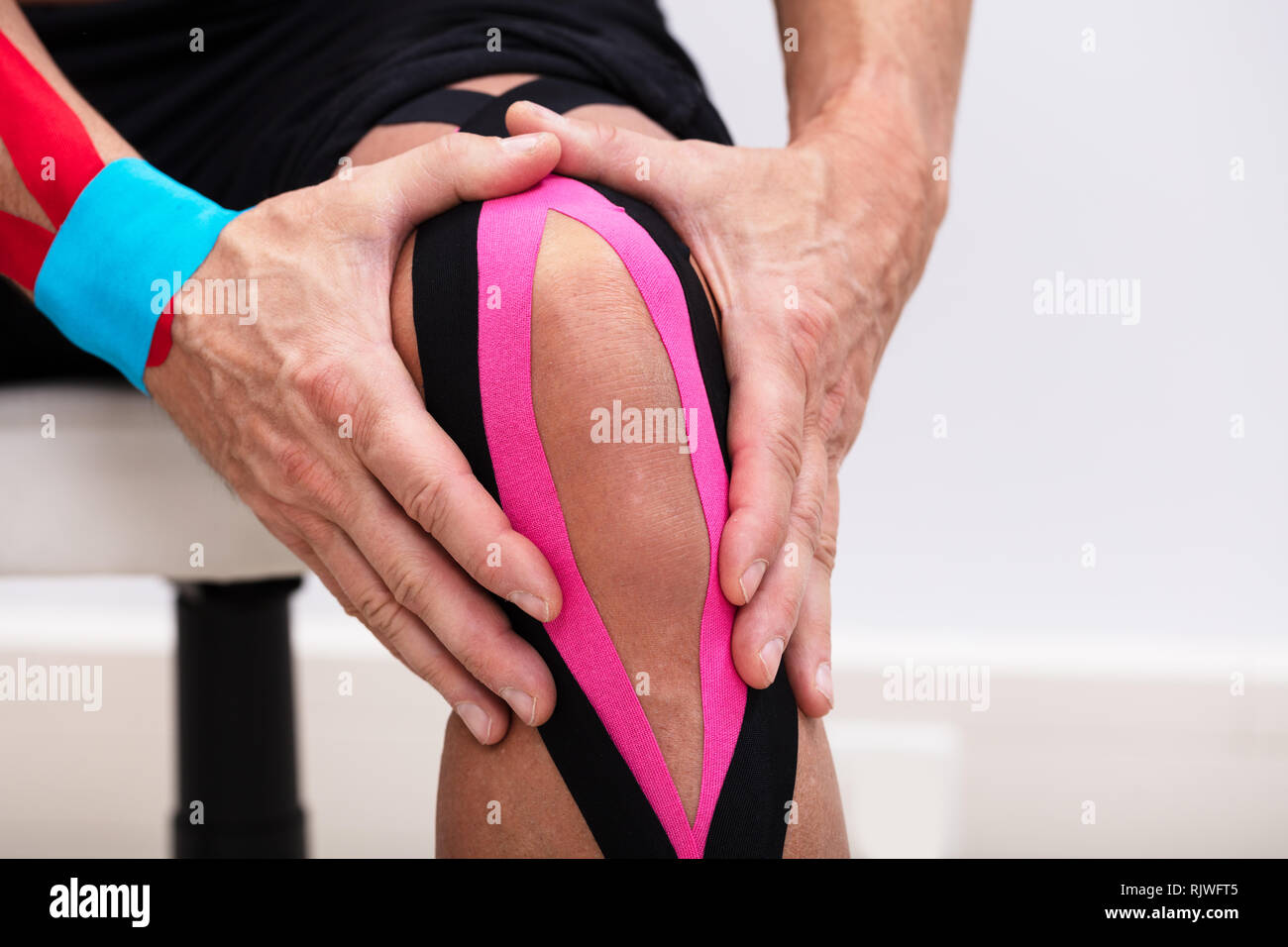 Homme assis sur la table l'application de la kinésiologie tape sur son genou Banque D'Images