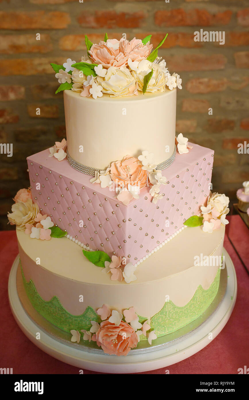 Gâteau à trois niveaux de forme différente pour événements officiels, mariages ou anniversaires, orné de fleurs et de sucre à glacer en velours et bijoux comestibles Banque D'Images