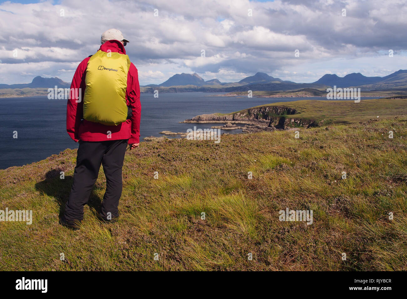 Un seul mâle rambler visualisation du paysage sur la péninsule de Coigach Ecosse, portant un manteau rouge et un sac à dos jaune couverts, avec les montagnes et la mer. Banque D'Images