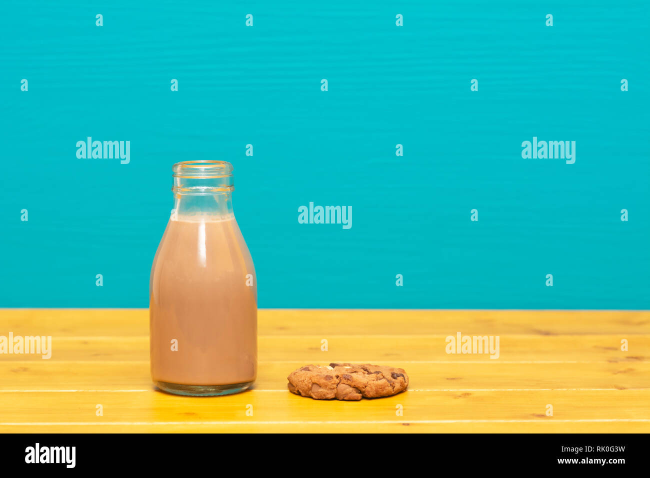 Lait frappé au chocolat dans un style rétro un tiers de pinte de lait en verre bouteille et d'un biscuit aux brisures de chocolat, sur une table de bois contre un lumineux peint sarcelles backgroun Banque D'Images
