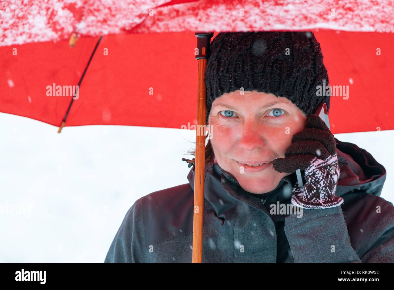 Happy Woman talking on mobile phone sous parapluie rouge tout en se tenant dans la rue en hiver neige Banque D'Images