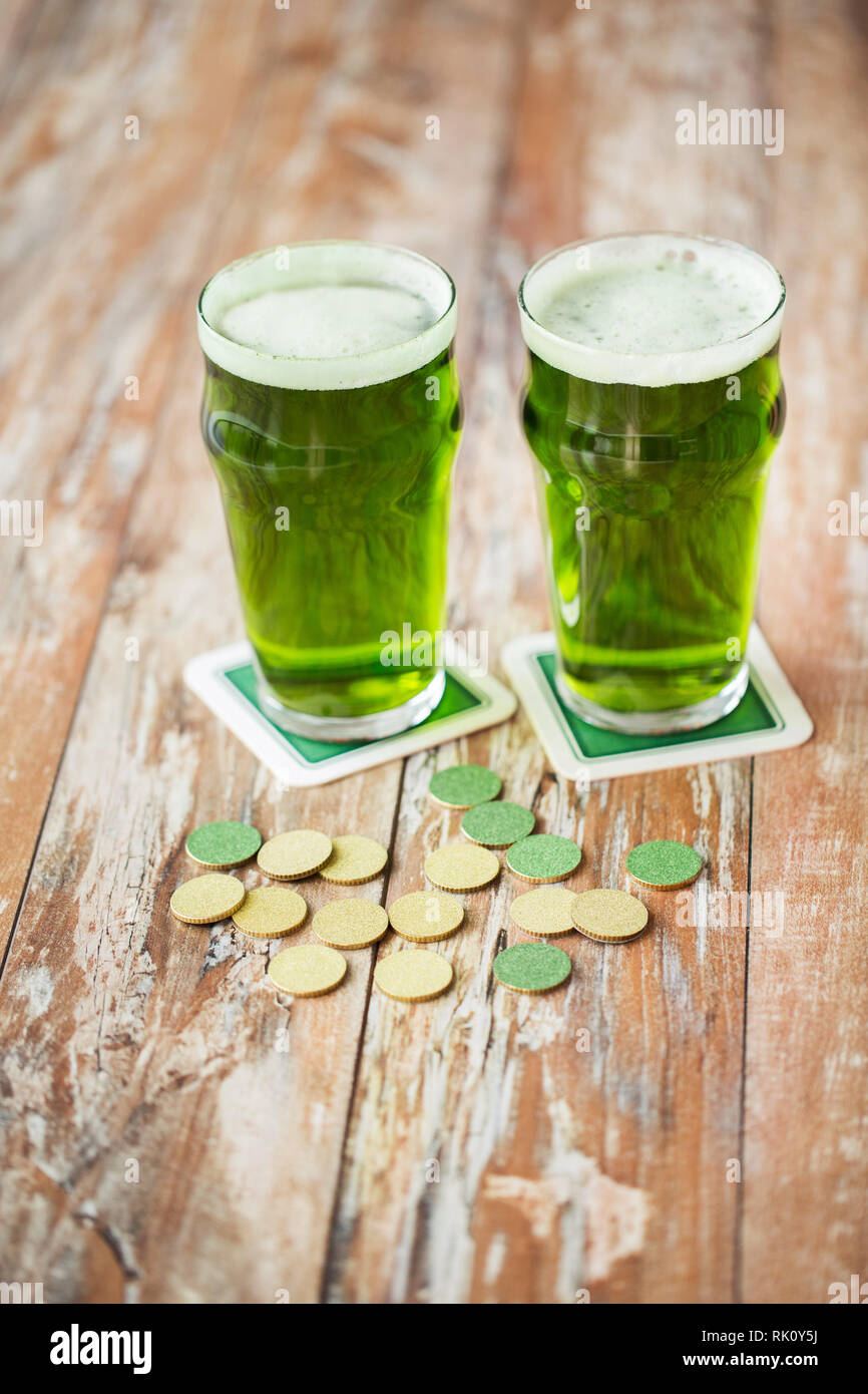Verres de bière verte et de pièces d'or sur la table Banque D'Images