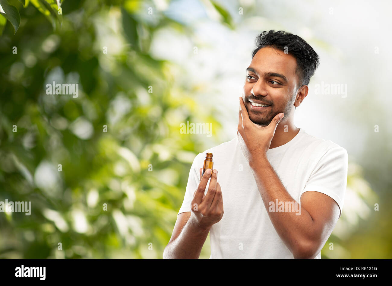 Smiling indian man l'application d'huile sur la barbe de toilettage Banque D'Images