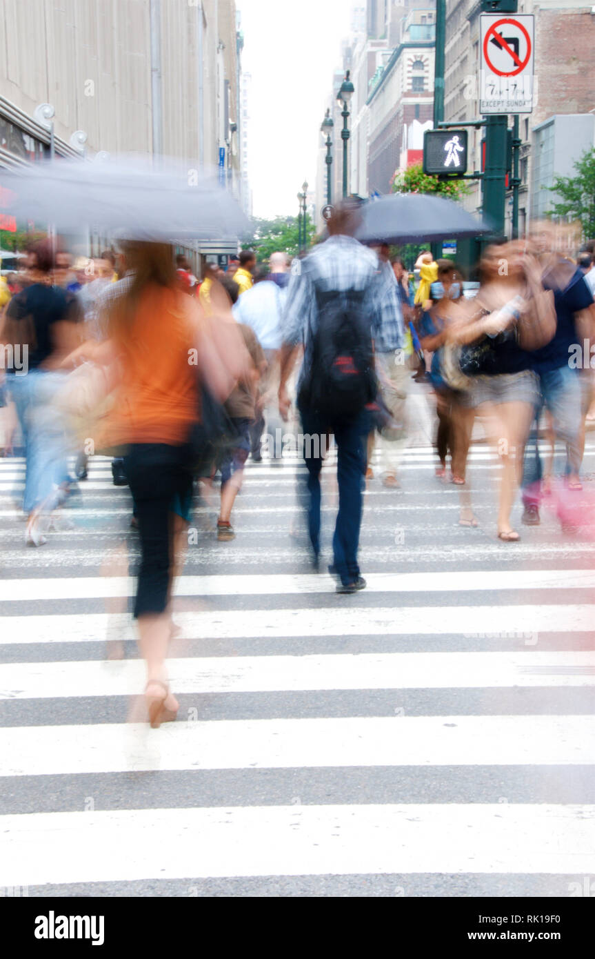 Hommes et femmes, certains tenant un parapluie, traversant une voie piétonne dans une section urbaine animée flanquée de grands bâtiments. Banque D'Images