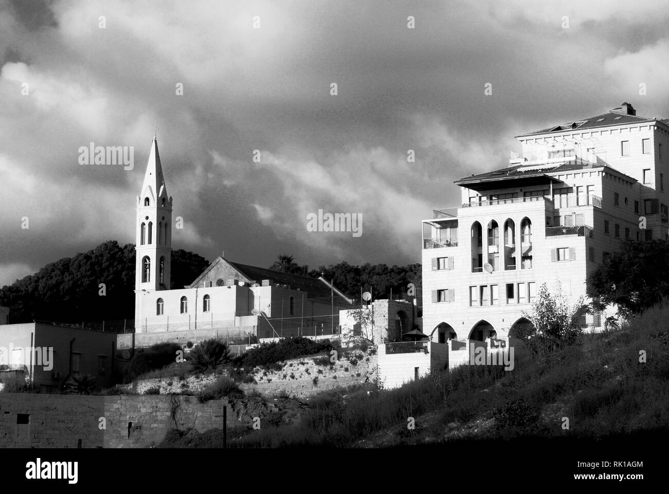 Vue urbaine de midi d'une église et d'une architecture intéressante maison avec 4 étages, d'un balcon et d'arches, sous un ciel nuageux, en noir et blanc. Banque D'Images