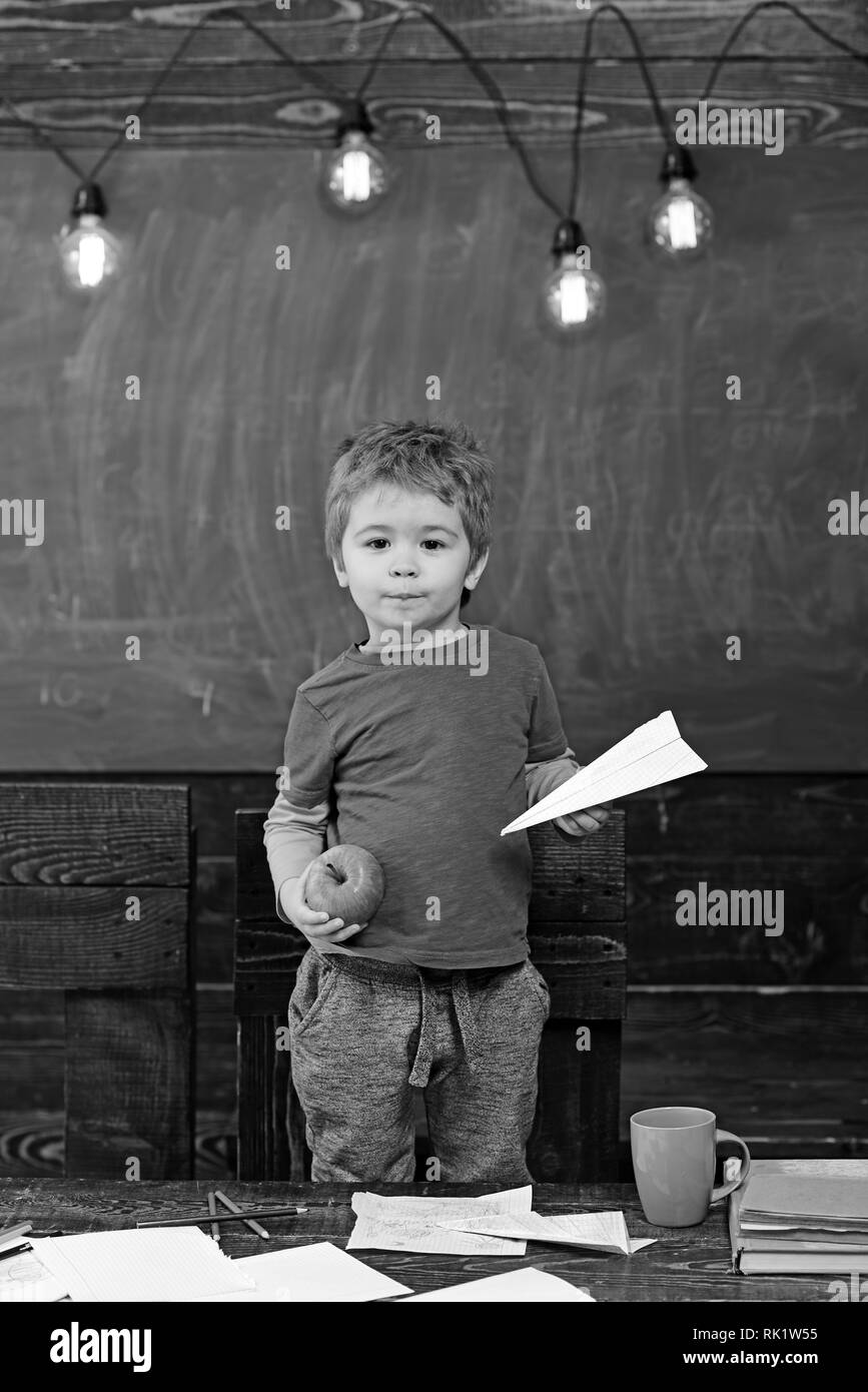 Little Boy holding paper plane et apple dans ses mains. Écolier en bleu T-shirt debout derrière la table. Concept jeu éducatif Banque D'Images