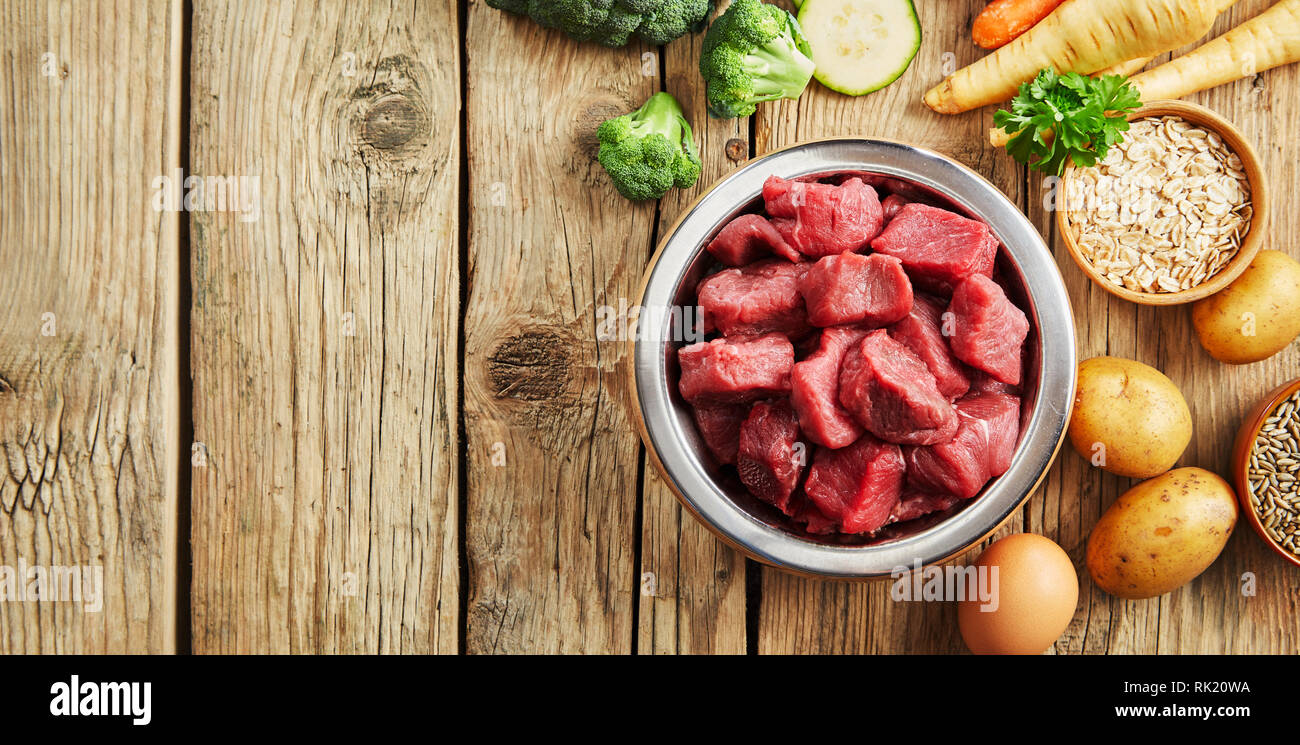 Bol de viande hachée pour un chien ou un chat sur un sol en bois rustique entouré par des légumes frais pour la santé de l'alimentation animale Banque D'Images