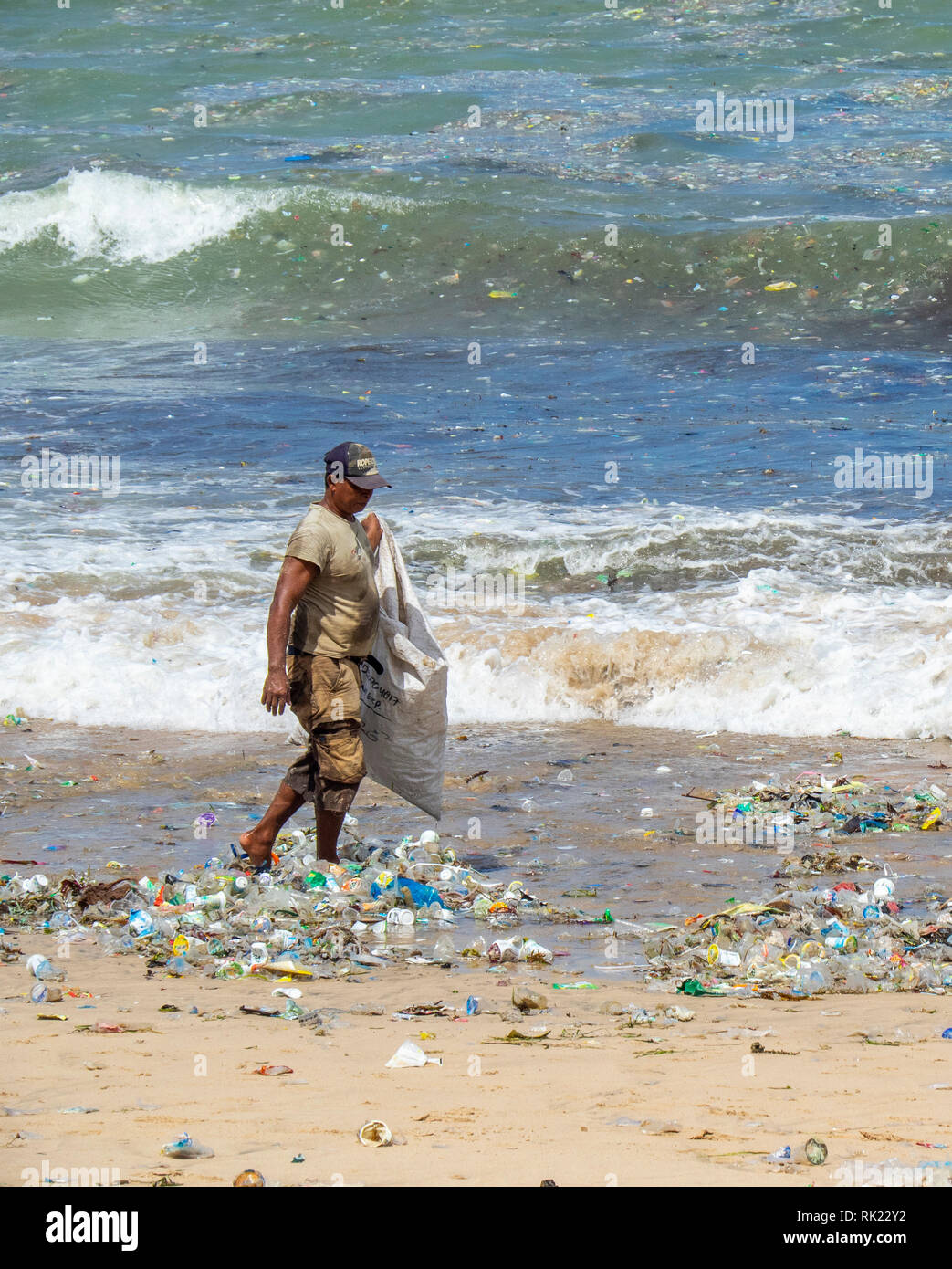 La pollution, l'homme seul ramasser des bouteilles en plastique, des tasses, des pailles et autres détritus échoués sur la plage de La Baie de Jimbaran, Bali Indonésie.. Banque D'Images
