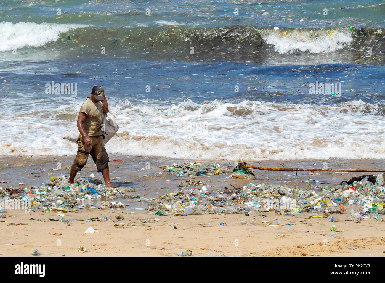 La pollution, l'homme seul ramasser des bouteilles en plastique, des tasses, des pailles et autres détritus échoués sur la plage de La Baie de Jimbaran, Bali Indonésie.. Banque D'Images