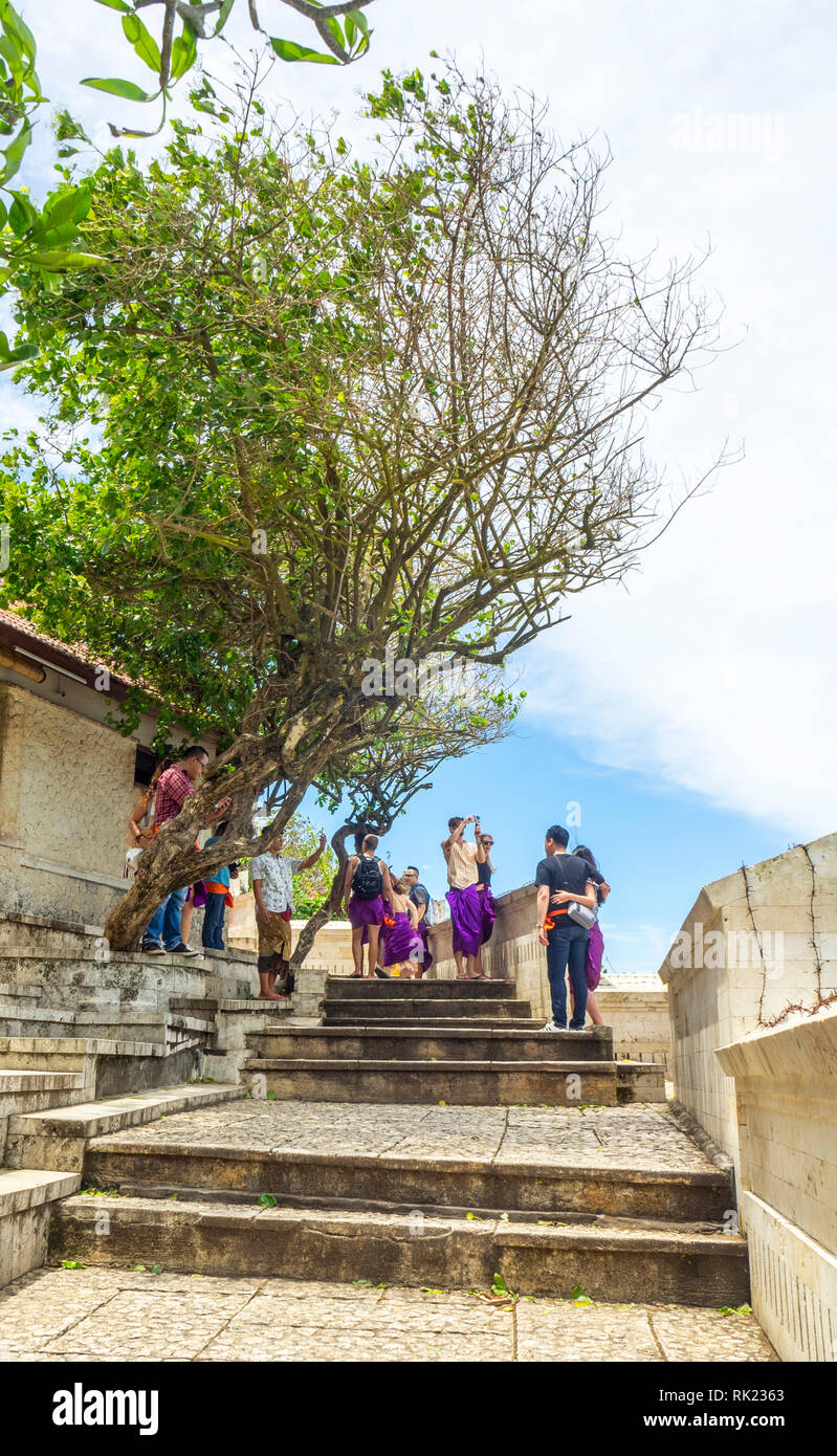 Les touristes chinois portant des jupes violet visiter Temple d'Uluwatu Bali Indonésie. Banque D'Images