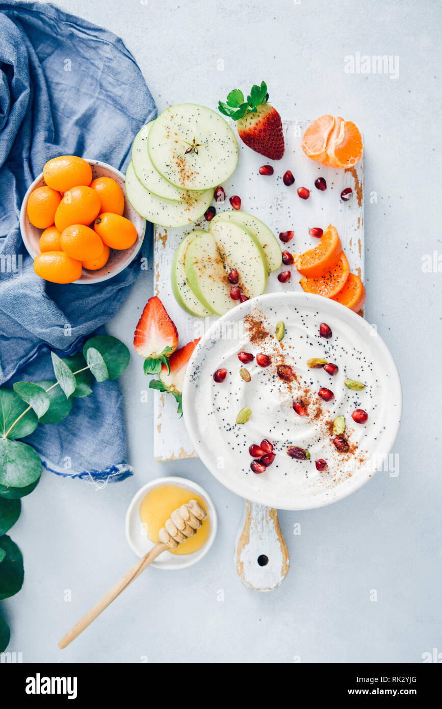 Fruits yogourt garni de tremper les graines de pavot, de grenade, les arilles de pistaches et la cannelle dans un bol en céramique blanche sur une planche de bois blanc. Banque D'Images