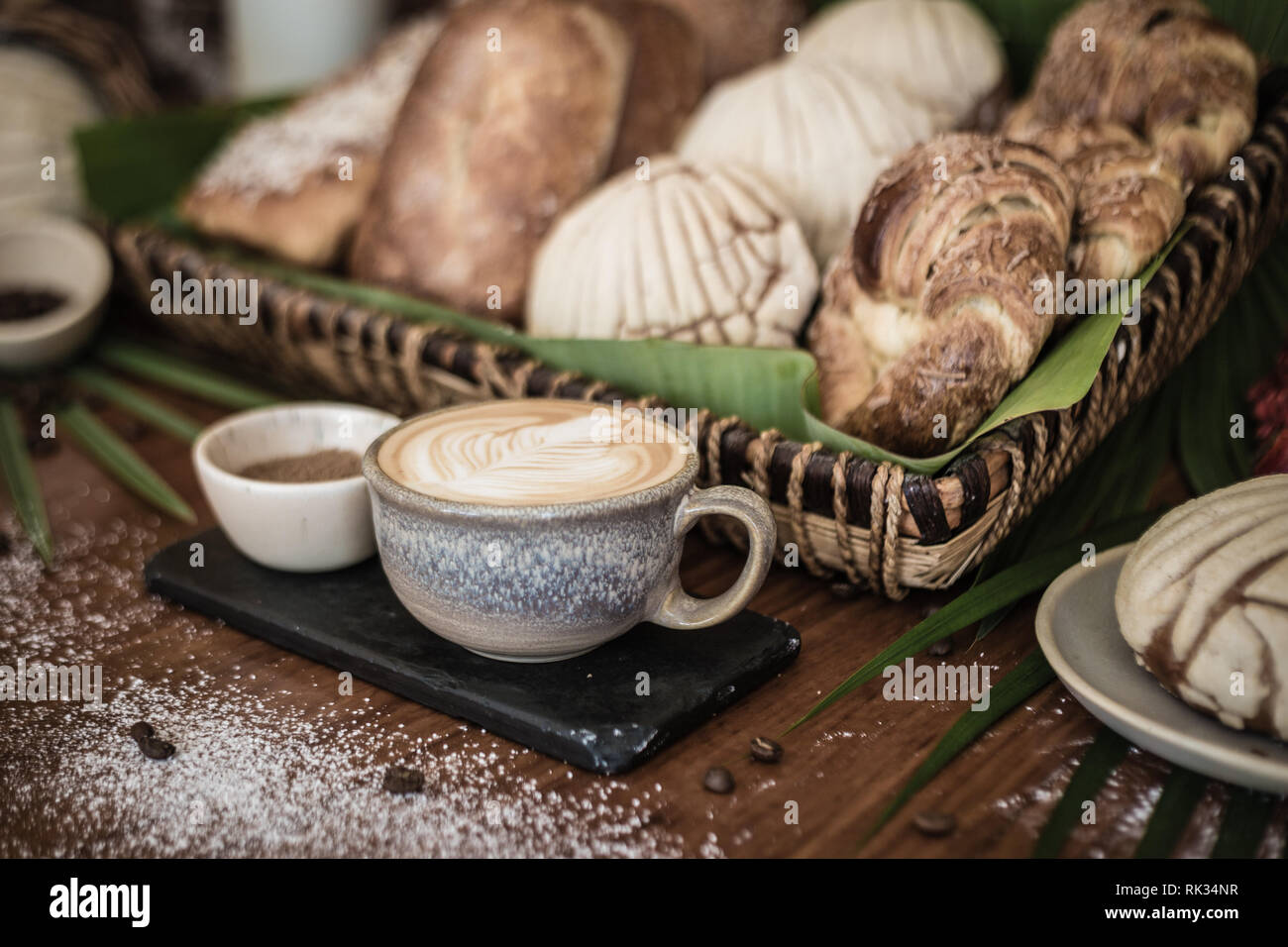 Le café et le sucre sur le carrelage avec un panier de viennoiseries, de bois et de feuilles de palmier Banque D'Images