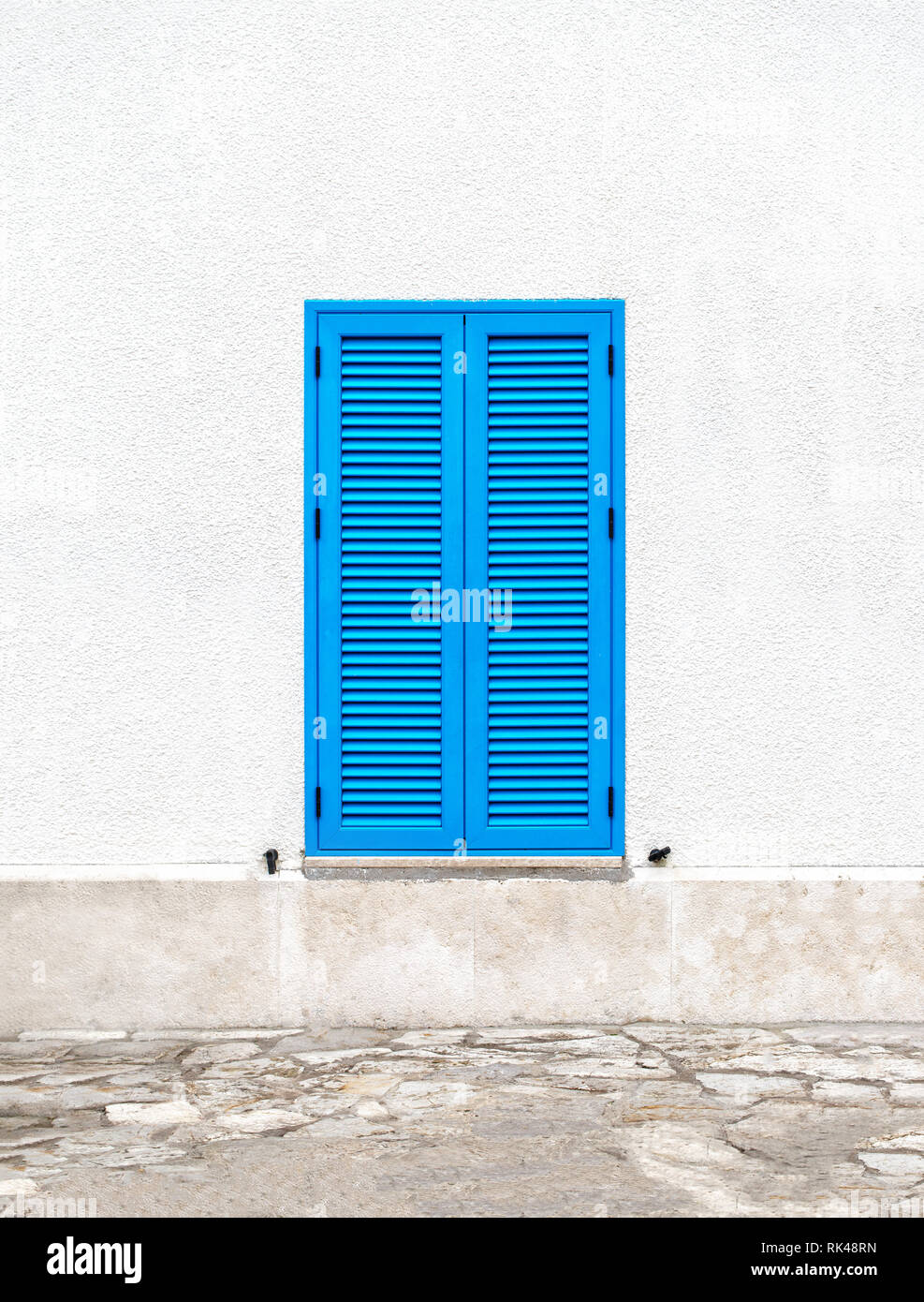 Une fenêtre avec des volets bleus sur un mur blanc dans le style grec de la ville de Santorini sur une journée ensoleillée. Banque D'Images
